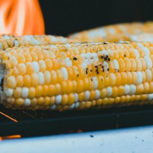 Close-up of corn on the cob grilling with flames on a barbecue.